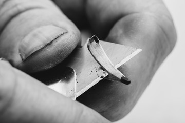 Elderly man sharpens pencil with clerical knife. Fingers of old man close up in grayscale....