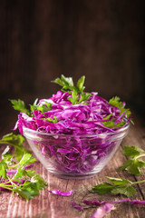 Shredded red cabbage with parsley in a transparent bowl on a dark wooden background, Vegetarian healthy food.