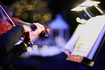 hands playing violin at concert with christmas lights in background bokeh