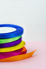 A stack of satin color rolls of bright blue, purple, yellow and green ribbons on a pink background for decoration and gift wrapping vertical