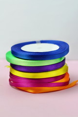 A stack of satin color rolls of bright blue, purple, yellow and green ribbons on a pink background for decoration and gift wrapping vertical