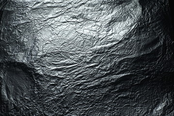 Thin wrinkled sheet of crushed tin aluminum silver foil background texture 