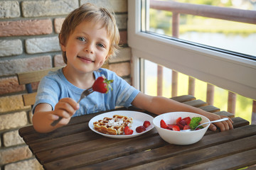 Happy 5 year old caucasian boy eat for Breakfast Viennese waffles with ice cream and strawberries
