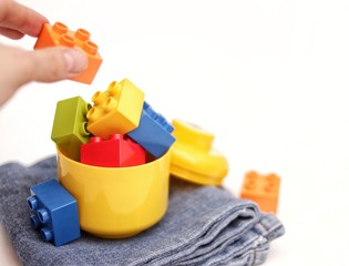 Toy colorful plastic blocks, bricks, stacked in thematic box, jeans, on a light background.