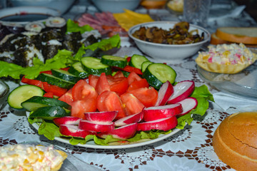 Tomatoes, cucumbers, radishes, sliced lie on a dish, dressed with olive oil for vegetarian food on a festive table.