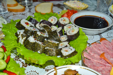 Sushi lay on the green leaves next to the soy sauce.