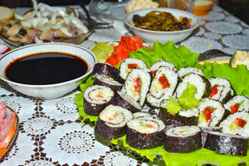 Sushi lay on the green leaves next to the soy sauce.
