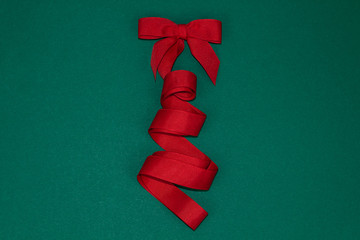 Christmas tree made of red ribbon on green background.