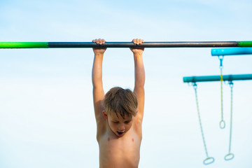 Fototapeta premium A little boy plays sports on a horizontal bar on the street, performs a workout in athletics.