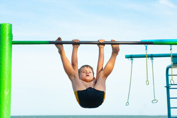 Fototapeta premium A little boy plays sports on a horizontal bar on the street, performs a workout in athletics.