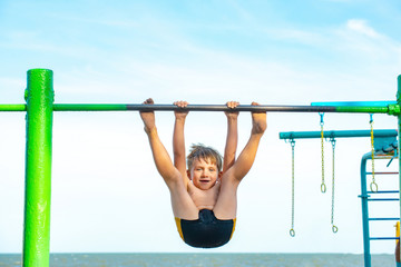 Fototapeta premium The boy on the uneven bars beats himself on the seashore, heavy exercise for the child.