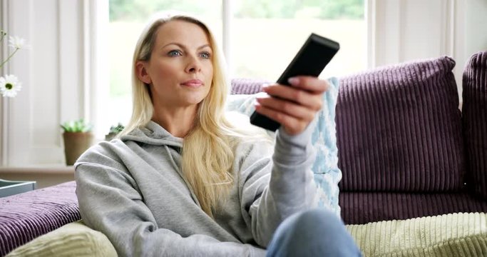 Beautiful Blond Woman Using TV Remote Control Sitting On Sofa