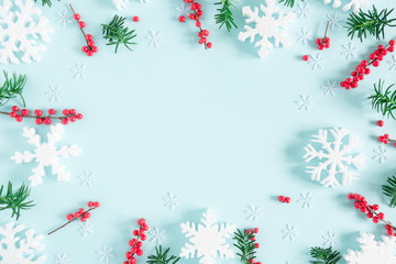 Fototapeta na wymiar Christmas modern composition. Frame made of green fir tree branches, red berries and snowflakes on pastel blue background. Christmas, New Year, winter concept. Flat lay, top view, copy space