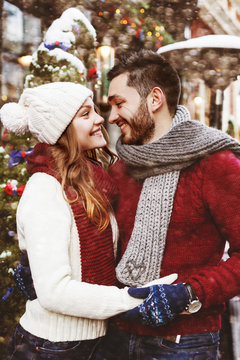Young happy smiling couple posing on street. Models looking at each other, wearing stylish warm knitted sweaters, scarves, gloves, hat