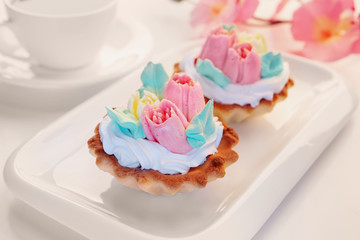 Delicious small round sand cakes with whipped cream for eating lie on a white dish. Cakes-baskets decorated with cream in the form of tulips. Photography in high key selective focus, Studio.