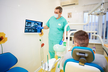 a man sits in the dentist's chair and looks at the monitor, near which stands the dentist