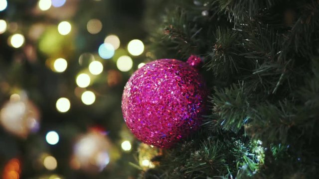 Christmas card. Christmas picture. A bright sparkling pink ball on the fluffy branches of a Christmas tree. Background bokeh lights of garland. Ready Christmas background for your text. Glitter.