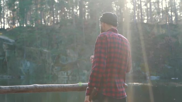 Bearded man stand in the forest near lake and whatching an amazing view. A man with an ax.