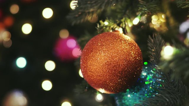 Christmas card. Christmas picture. Bright sparkling orange ball on the fluffy branches of a Christmas tree. Background bokeh lights of garland. Ready Christmas background for your text. Glitter.