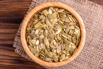 Fresh pumpkin seeds in wooden bowl with burlap napkin