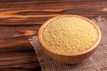 Raw couscous grain in wooden bowl with burlap napkin