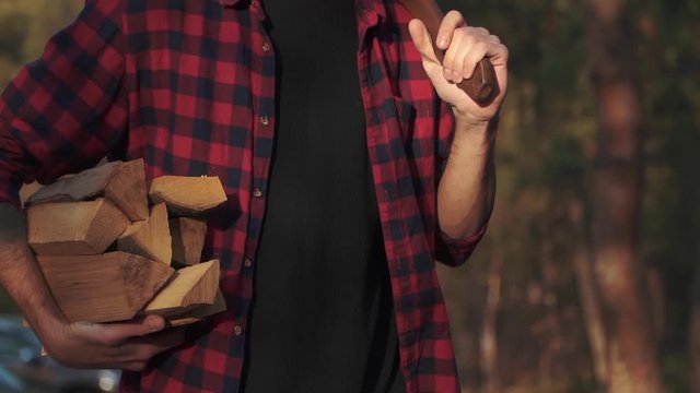 Bearded guy walk in the forest with chopped logs in one hand and axe in his shoulder. Forester carries firewood.