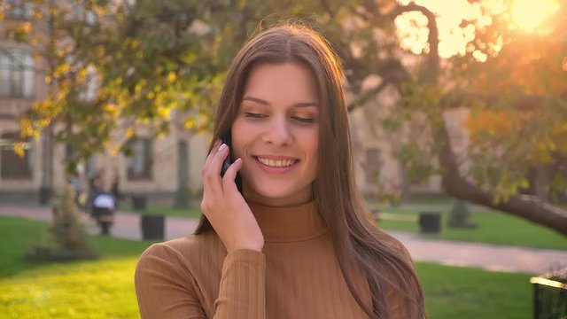Portrait of attractive brunette gerl talking on cellphone on green park background.