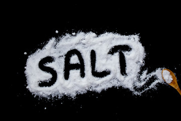 The word salt written into a pile of white salt and salt shaker on black background