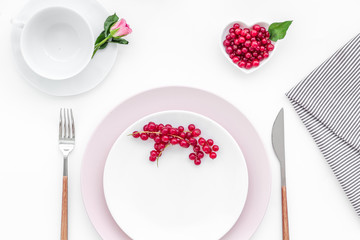 Simple color table setting for celebration with roses, wineberry, pink plates and heart-shaped saucers on white table background top view mock up