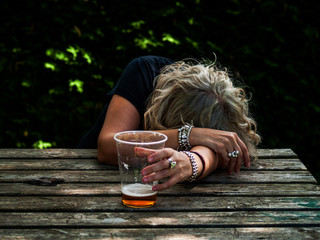 A drunk woman with a glass of beer in her hand, unconscious, leaning on a table