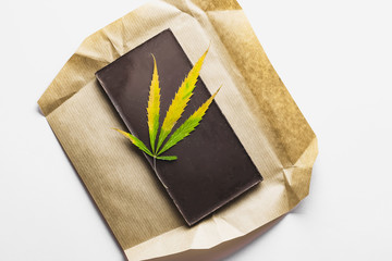 Marijuana leaf with edible dark chocolate block and cannabis brownie with ganja top view isolated on white background
