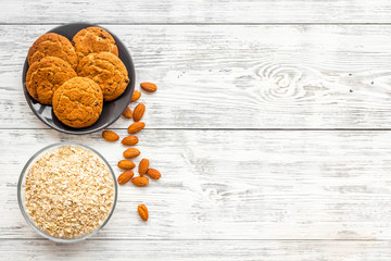 Ingredients for homemade oatmeal cookies. Fresh cookies near oatmeal and nuts on white wooden background top view copy space