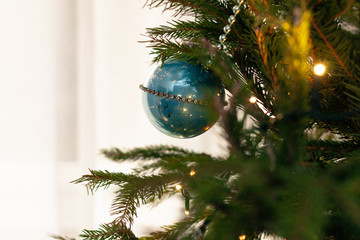 A blue bauble hanging on a Christmas tree backlit against a window