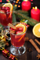 Mulled wine on a wooden background with candles, pine branches and Christmas lights. Selective focus