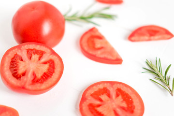 Fototapeta premium Slices of tomatoes on a white background. Frame for a banner with tomato and rosemary. White background with vegetables. View from above. Fresh tomatoes