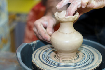 Potter's hands close-up with pot and pottery wheel.