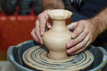Potter's hands close-up with pot and pottery wheel.