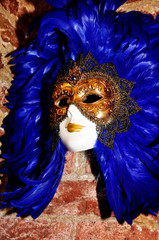 A real Venetian blue feather mask on a brick wall in the Artistic Murano Glass Gallery in Venice,...