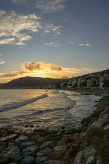 View from a rocky beach of a coastal city at sunset in winter, Alassio, Liguria, Italy
