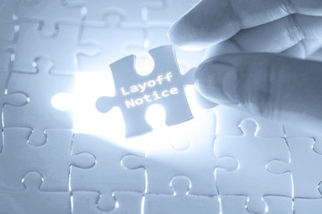 Businessman hand holding a jigsaw puzzle with layoff notice word. Business concept.