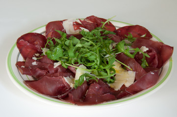 Piatto di bresaola con rucola e parmigiano in primo piano.  Tipico cibo italiano.