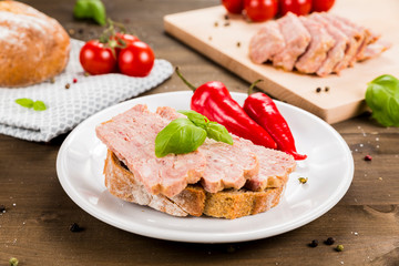Slice of bread with preserved ham and peppers. White plate on a wooden background
