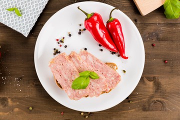 Slice of bread with preserved ham and peppers. White plate on a wooden background