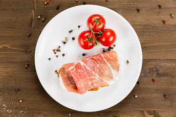 Slice of bread with preserved ham and ingredients. White plate on a wooden background