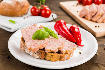 Slice of bread with preserved ham and peppers. White plate on a wooden background