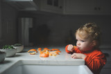 Blond girl eating orange by countertop in kitchen