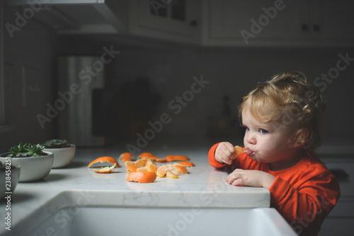 Blond girl eating orange by countertop in kitchen
