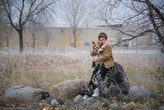 Boy with dog sitting on rock outdoors