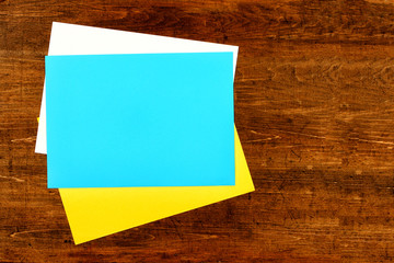 sheet of white, yellow and blue office paper lie on a wooden background, sticker on wooden table, copy space