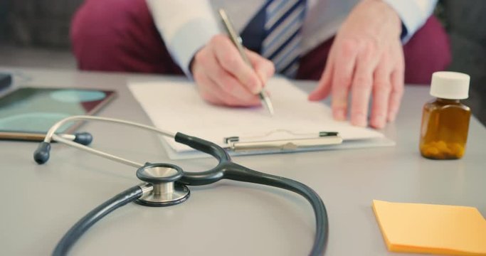 Male Doctor Filling Medical Form In Clipboard At Desk 4K